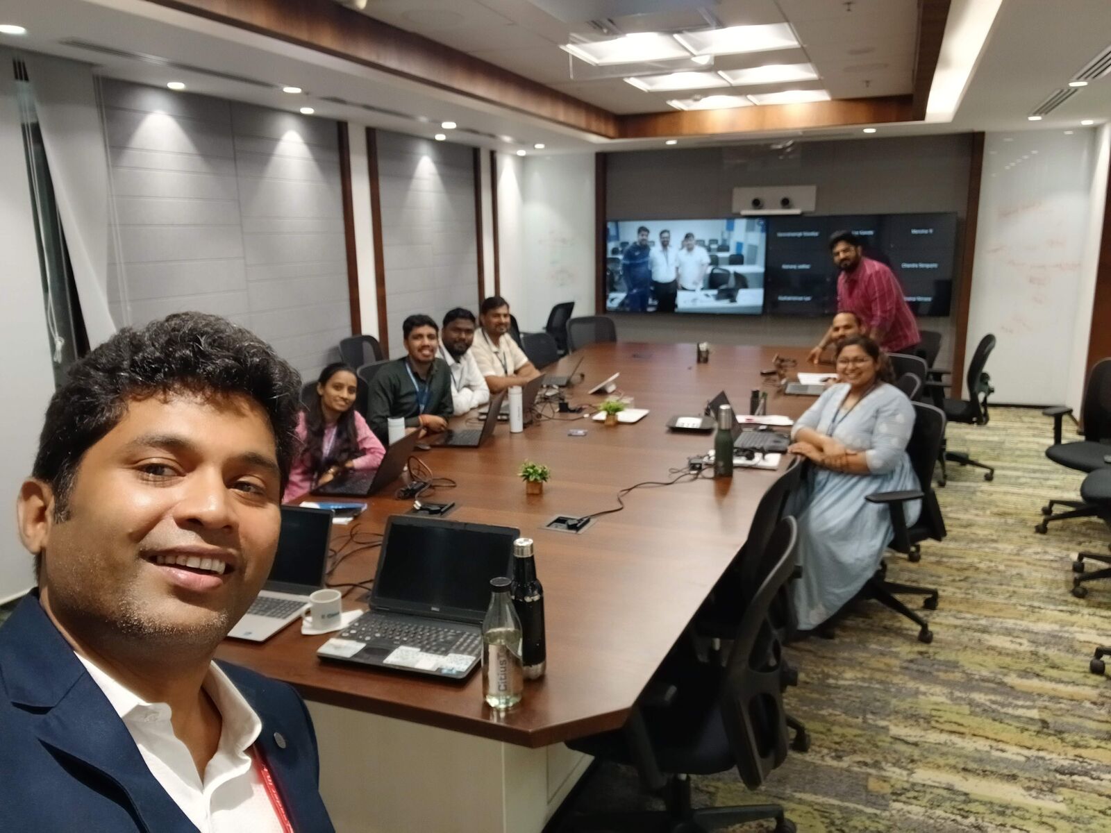 A trainer's selfie with the cohort working on laptops around the boardroom table during a session.